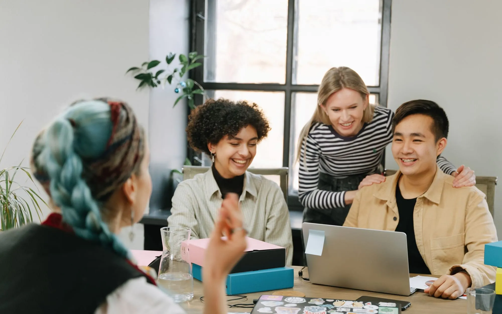 Colleagues laughing together around a laptop at a desk in a bright office